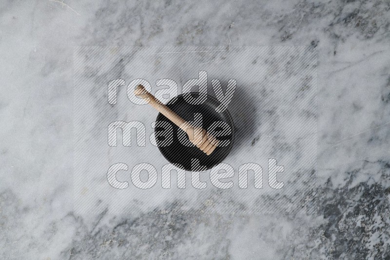 Black Pottery Bowl with wooden honey handle in it, on grey marble flooring, Top View