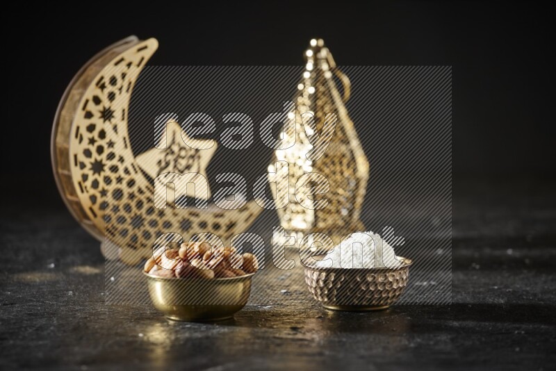Nuts in a metal bowl with desiccated coconuts beside golden lanterns in a dark setup