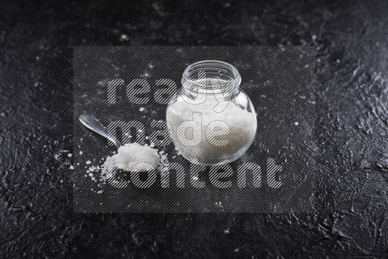 A glass jar full of coarse sea salt crystals on black background