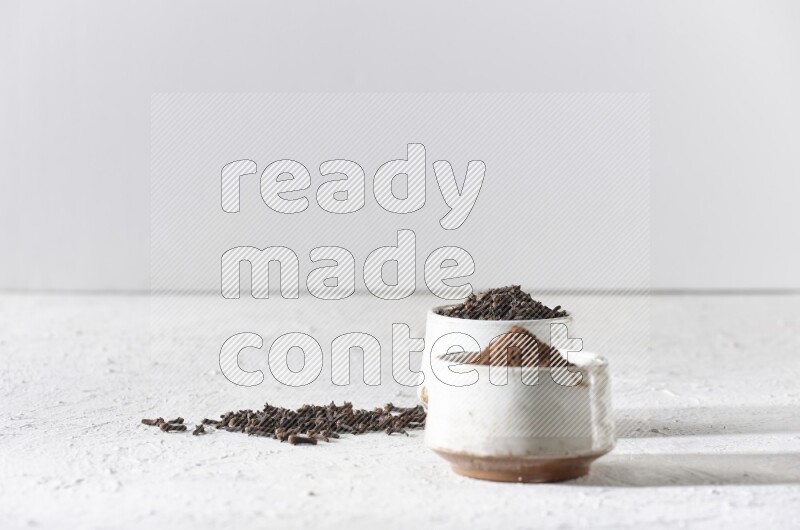 وعاءين من السيراميك بيج اللون، أحدهما مملوء بالقرنفل والآخر مملوء بالبودرة على أرضية بيضاء