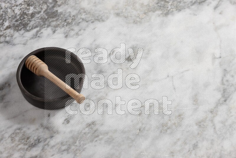 وعاء فخاري أسود مع ملعقة عسل خشبية بداخله على خلفية من الرخام الرمادي