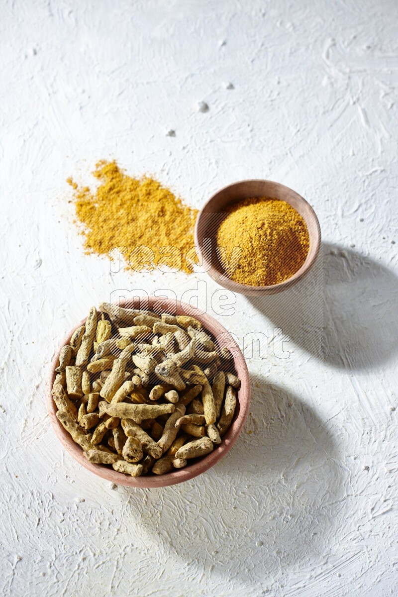 وعاءان خشبيان، أحدهما ممتلئ ببودرة الكركم والآخر بأصابع الكركم المجففة، على خلفية بيضاء