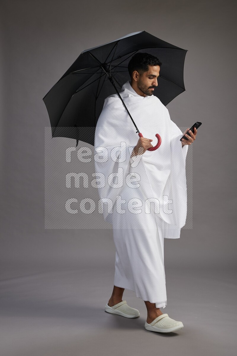 A man wearing Ehram Standing holding umbrella on gray background