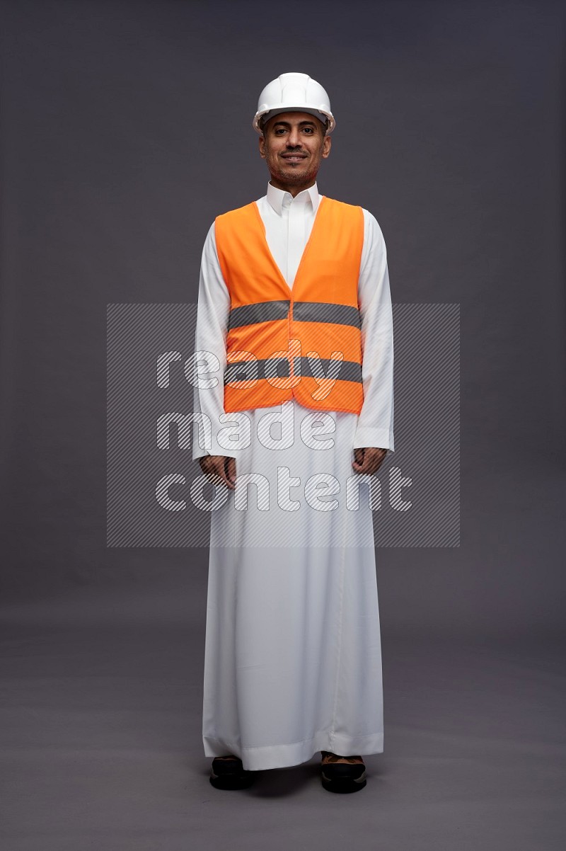 Saudi man wearing thob with engineer vest standing interacting with the camera on gray background