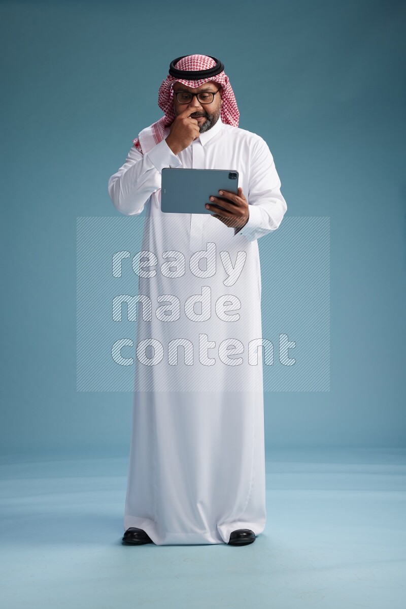 Saudi Man with shimag Standing holding a tablet on blue background