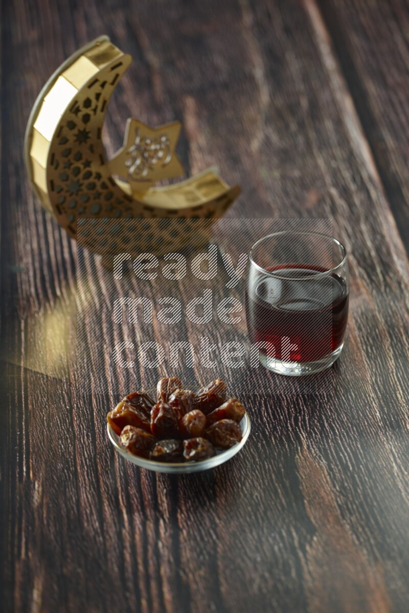 A wooden golden crescent lantern with different drinks, dates, nuts, prayer beads and quran on brown wooden background