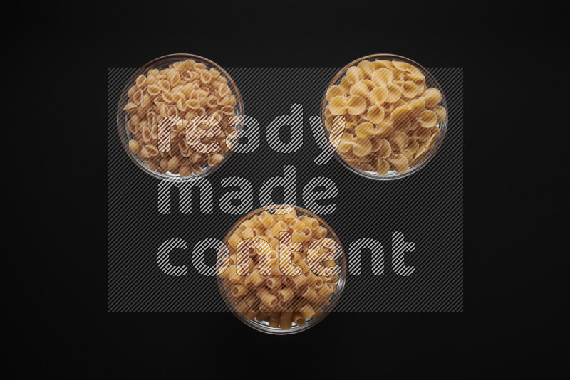 Different pasta types in glass bowls on black background