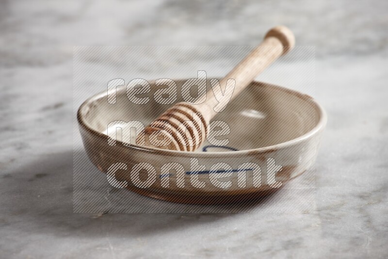 Multicolored pottery bowl with wooden honey dipper in it on grey marble background