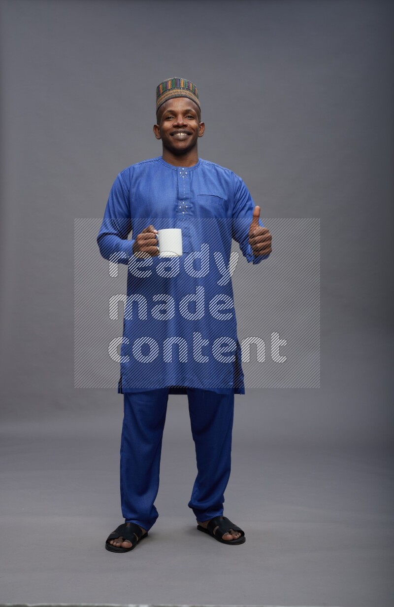 Man wearing Nigerian outfit standing holding mug on gray background