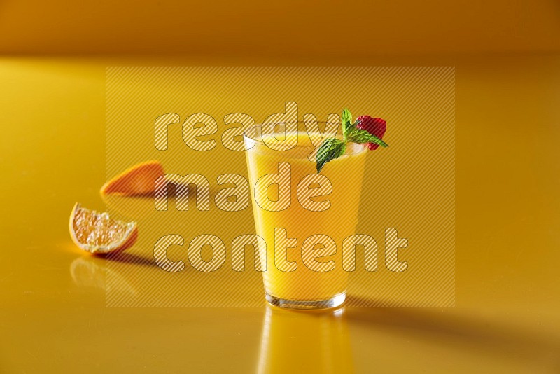 glass of orange juice with berry & mint on yellow background