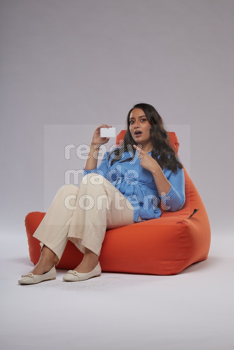 A woman sitting on an orange beanbag and holding ATM card