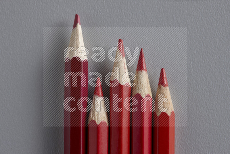 A collection of sharpened colored pencils arranged showcasing a gradient of red hues on grey background
