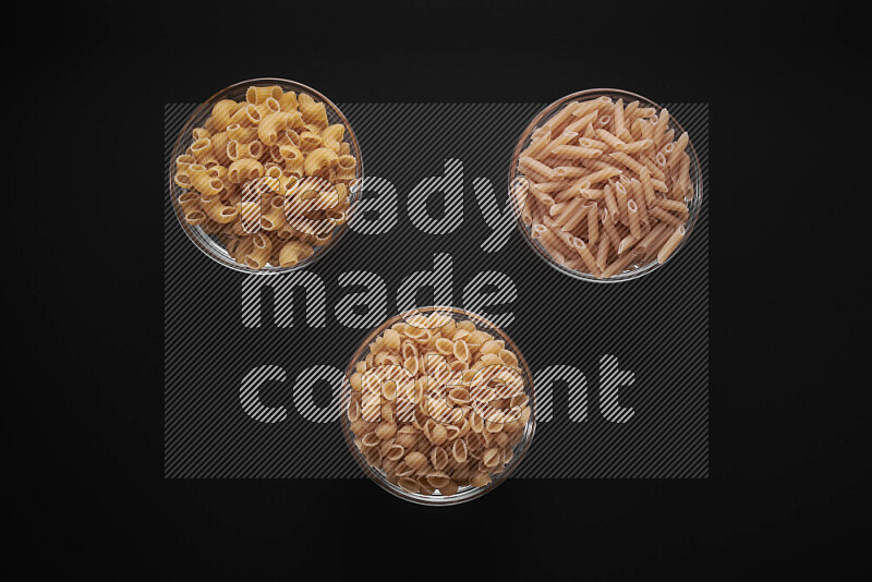 Different pasta types in glass bowls on black background