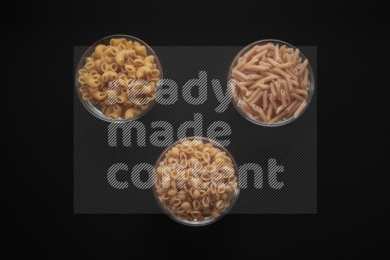 Different pasta types in glass bowls on black background