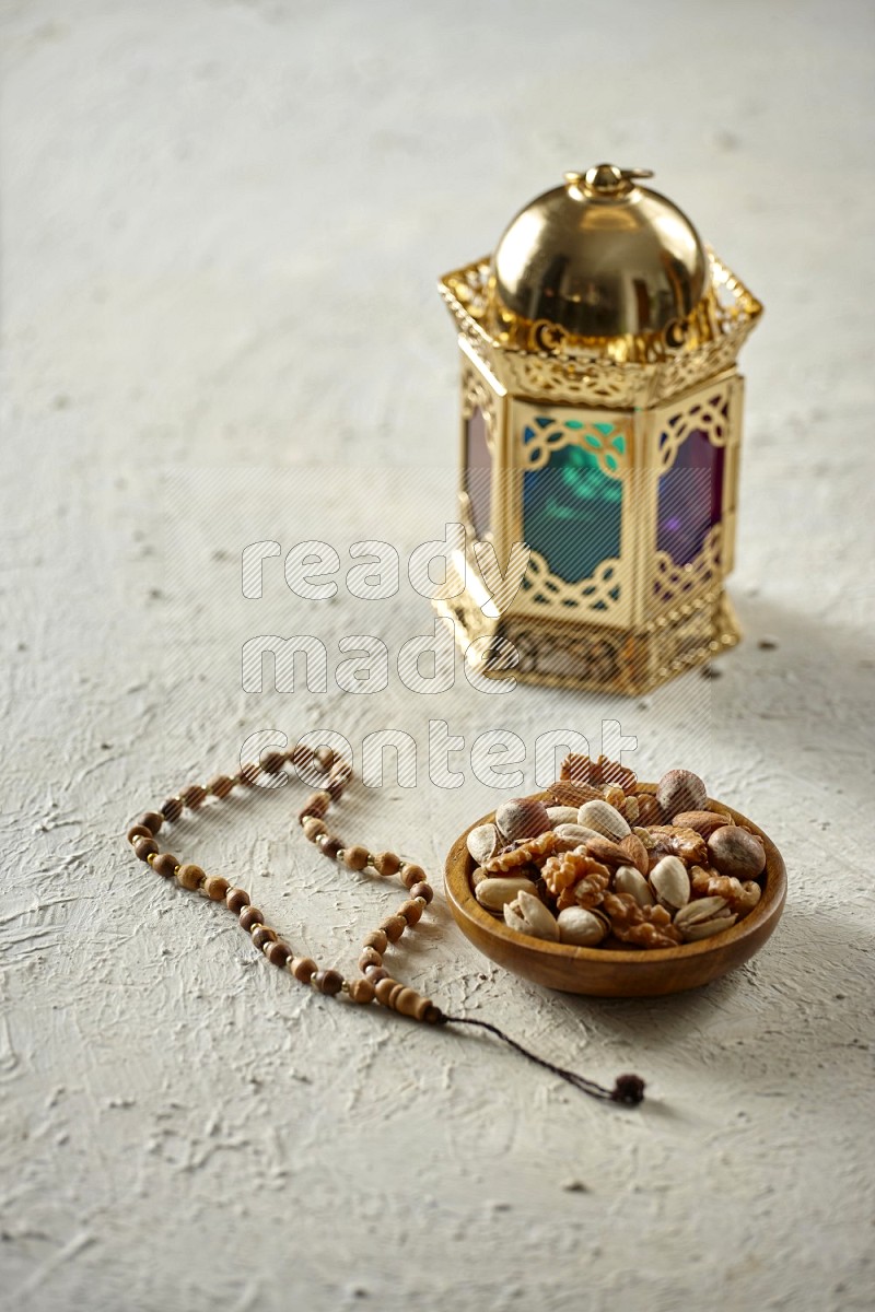 A golden lantern with different drinks, dates, nuts, prayer beads and quran on textured white background