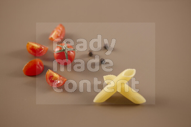 Raw pasta with different ingredients such as cherry tomatoes, garlic, onions, red chilis, black pepper, white pepper, bay laurel leaves, rosemary and cardamom on beige background