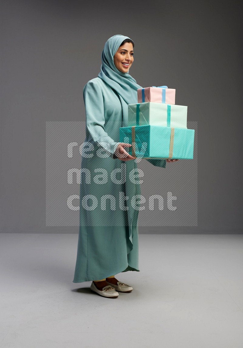 Saudi Woman wearing Abaya standing holding gift box on Gray background