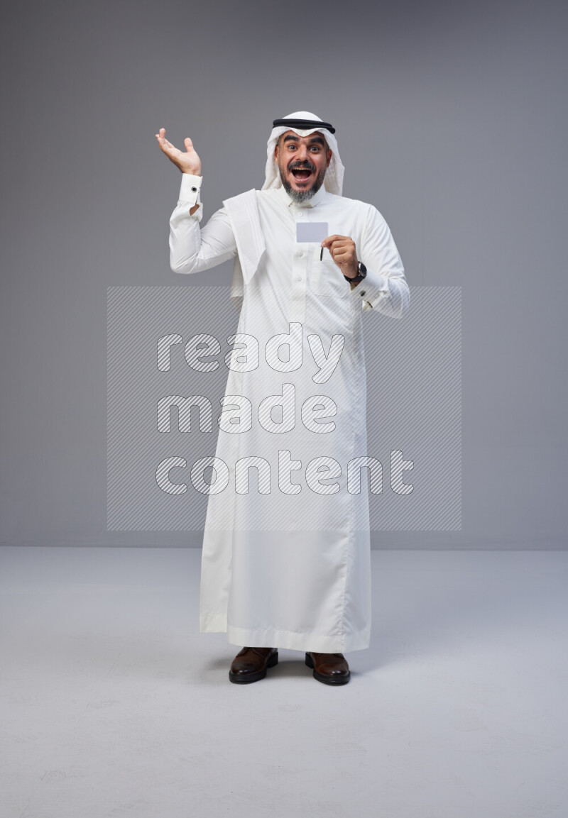Saudi man Wearing Thob and white Shomag standing holding ATM card on Gray background