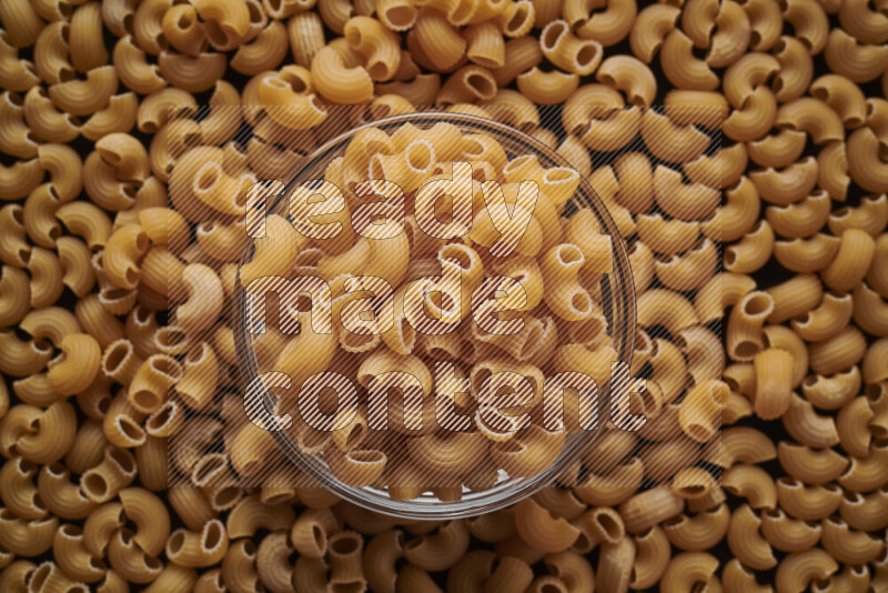 Elbow pasta in a glass bowl on black background