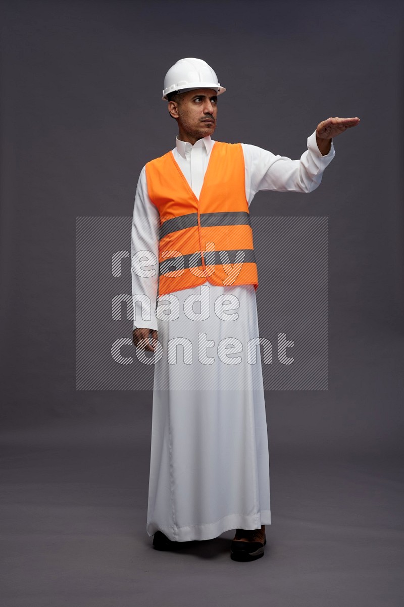 Saudi man wearing thob with engineer vest standing interacting with the camera on gray background