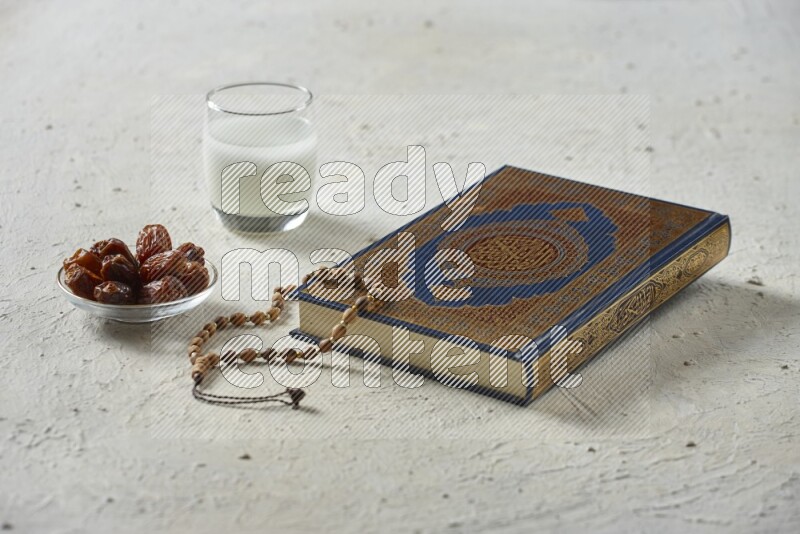 Quran with dates, prayer beads and different drinks all placed on textured white background