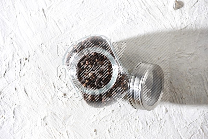 A glass spice jar full of cloves on textured white flooring