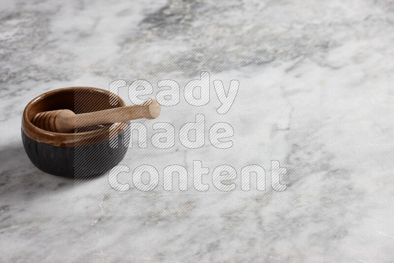 Multicolored pottery bowl with wooden honey dipper in it on grey marble background