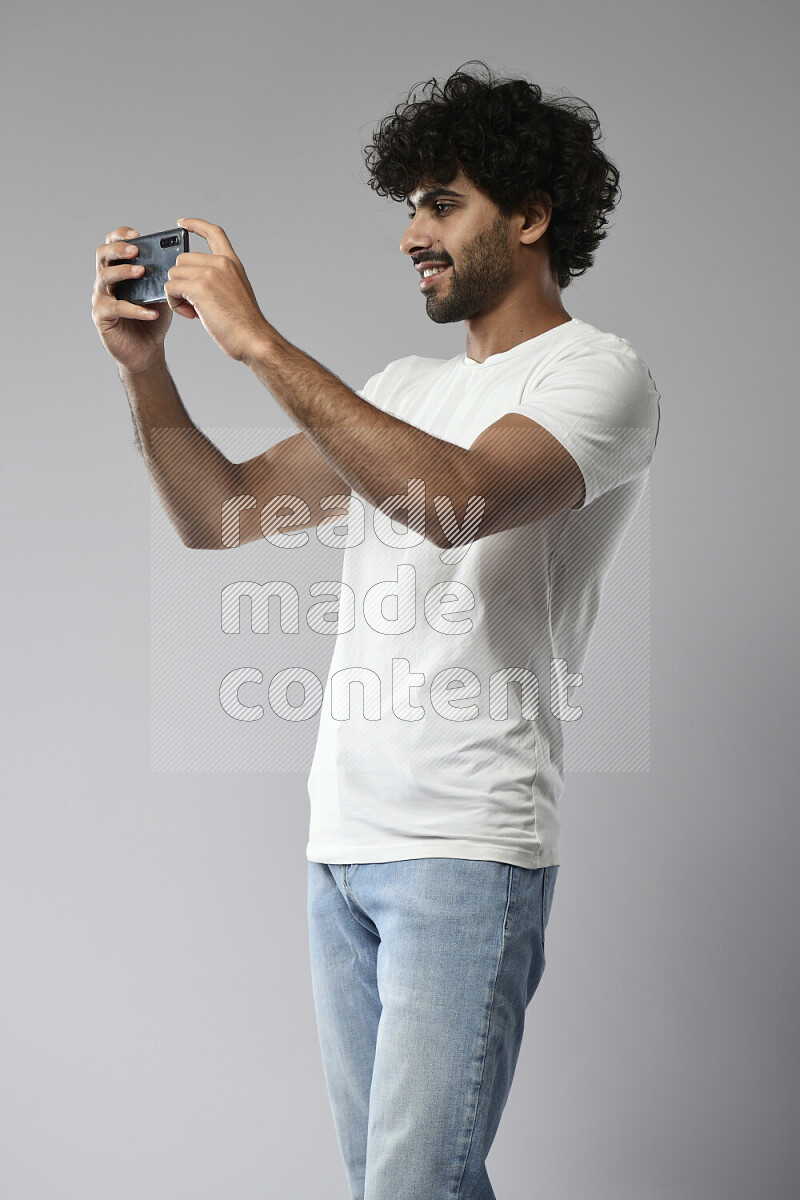 A man wearing casual standing and shooting with his phone on white background