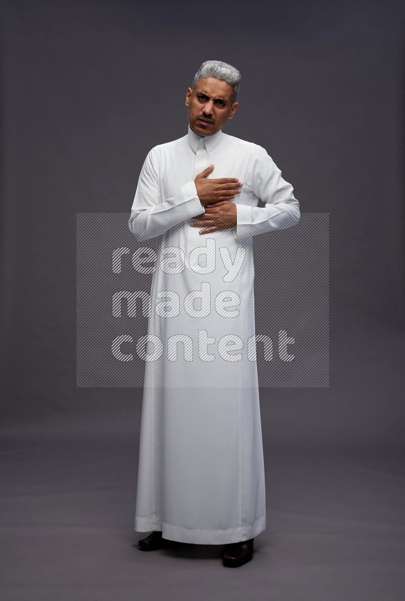 Saudi man wearing thob standing interacting with the camera on gray background