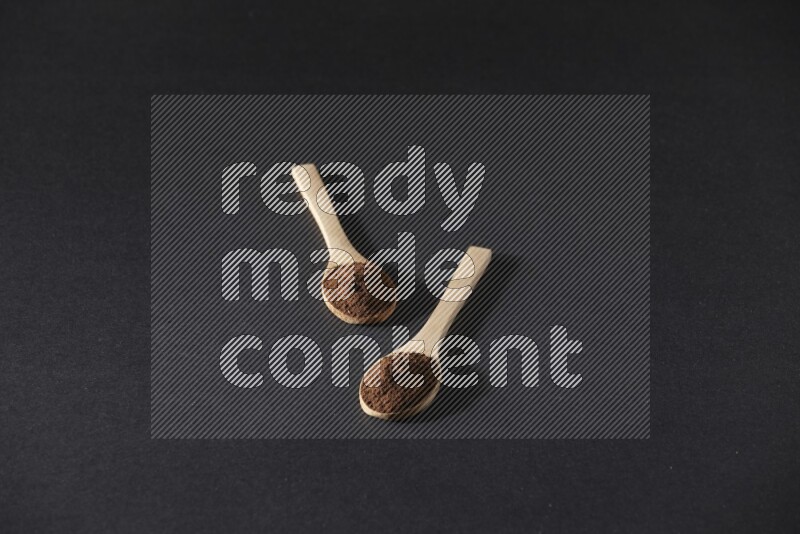 2 wooden spoons full of cloves powder on a black flooring