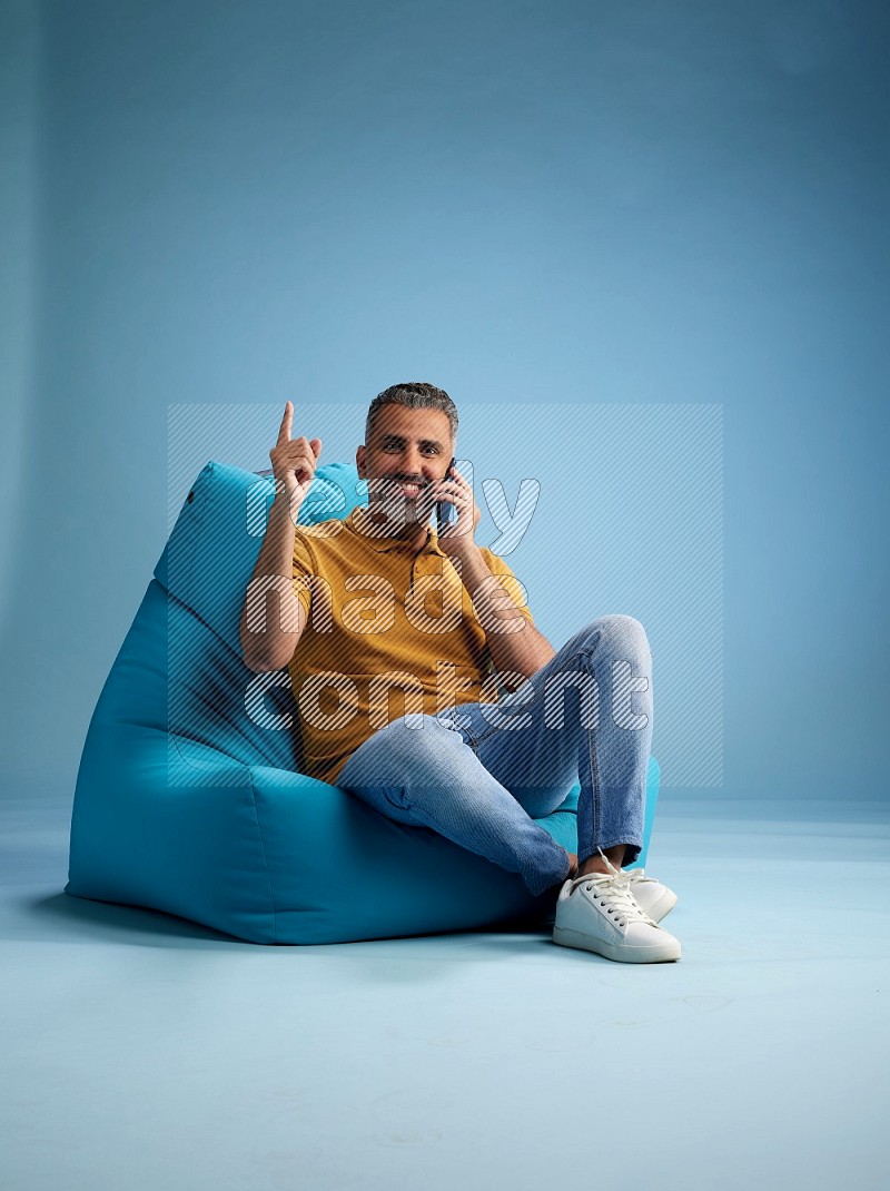 A man sitting on a blue beanbag and talking on the phone