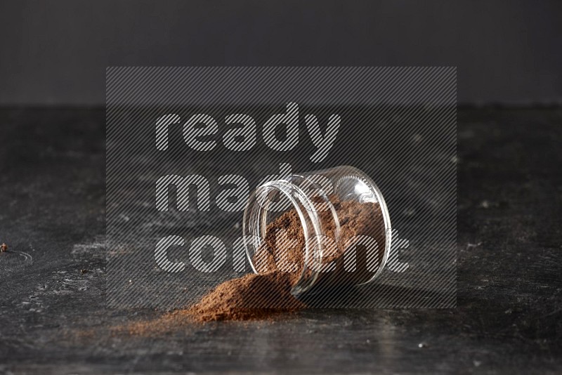 A flipped glass jar full of cloves powder on a textured black flooring