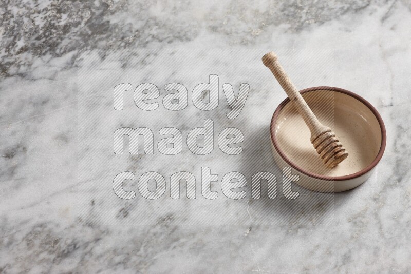 Beige Pottery oven bowl with wooden honey handle on the side with grey marble flooring, 65 degree angle
