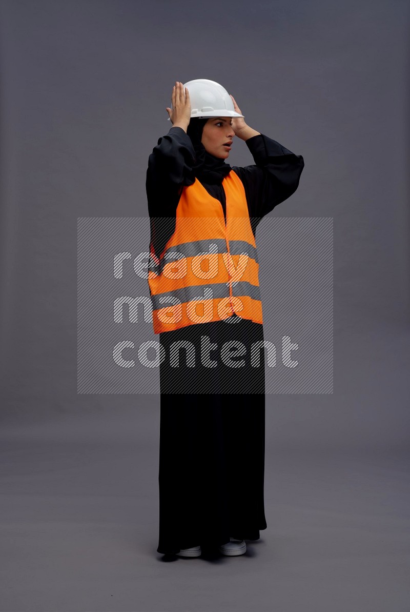 Saudi woman wearing Abaya with engineer vest standing interacting with the camera on gray background