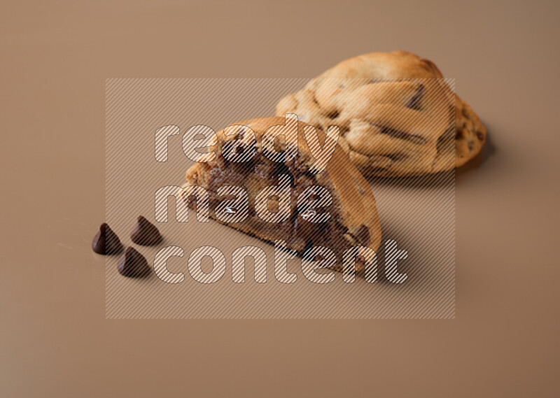 a chocolate chip cookie with another one cut in half on a brown background