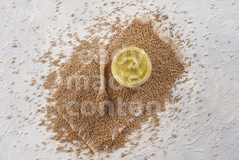 وعاء زجاجي ممتلئ بمعجون الخردل موضوع على قطعة من القماش مع ملعقة خشبية ممتلئة ببذور الخردل على خلفية بيضاء