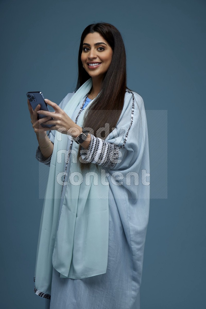 A Saudi woman Texting in a blue background wearing blue Abaya with no hijab