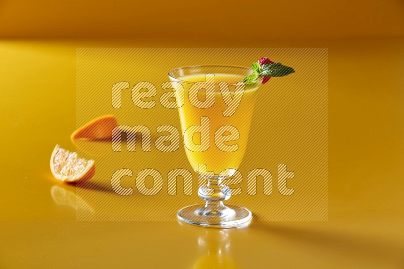 glass of orange juice with berry & mint on yellow background