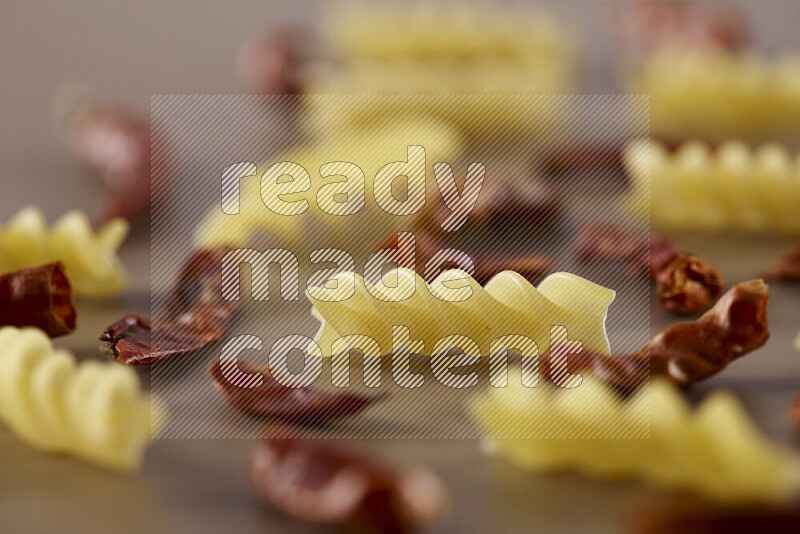 Raw pasta with different ingredients such as cherry tomatoes, garlic, onions, red chilis, black pepper, white pepper, bay laurel leaves, rosemary and cardamom on beige background