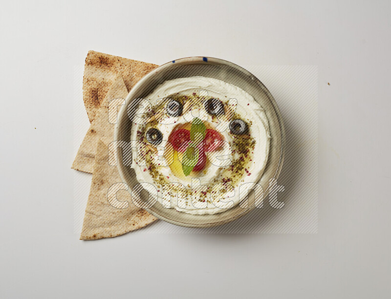 Lebnah garnished with cherry tomato, mint, olives & pine nuts in a grey pottery plate on a white background
