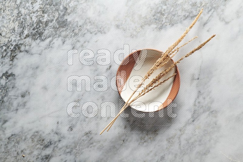 Wheat stalks on Multicolored Pottery Plate on grey marble flooring, Top view