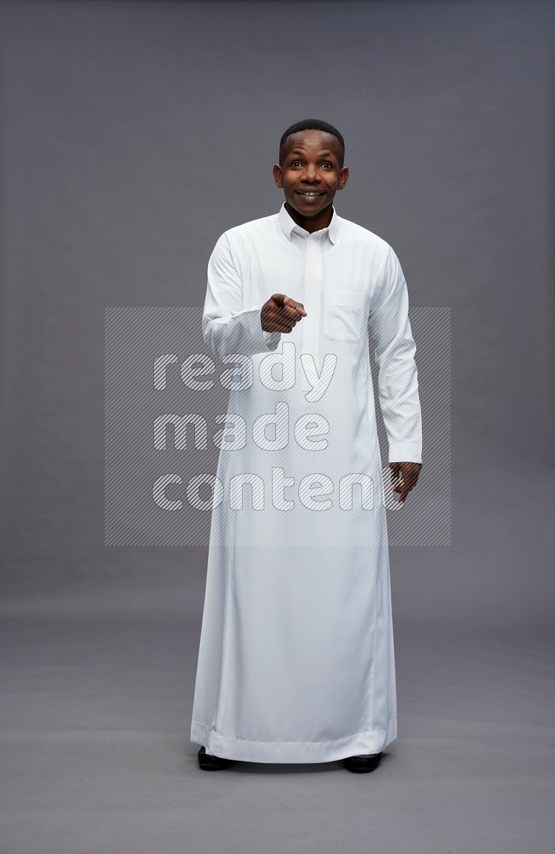 Saudi man wearing thob standing interacting with the camera on gray background