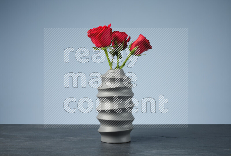 An arrangement of vivid red roses in a grey spiral vase on black marble background
