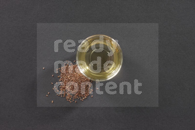 وعاء زجاجي ممتلئ بزيت بذر الكتان مع بعض حبوب بذر الكتان بجانبه علي خلفية سوداء