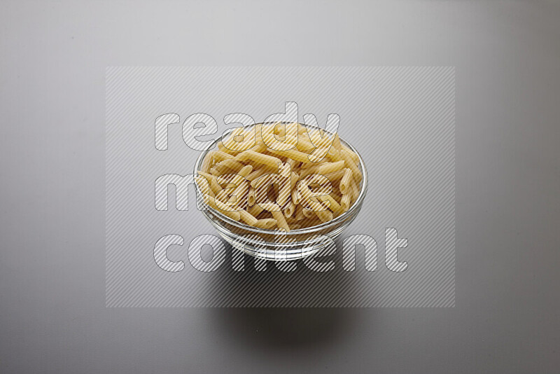 Mini penne pasta in a glass bowl on grey background