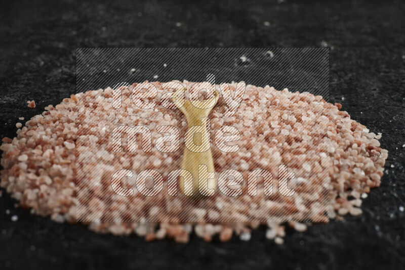 A wooden spoon full of coarse himalayan salt crystals on a bunch of the crystals on black background