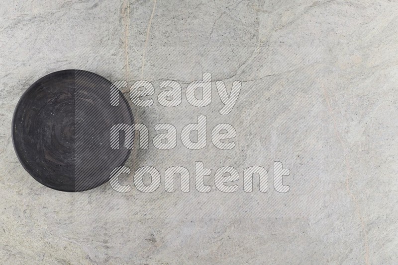 Top View Shot Of A Black Pottery Circular Plate On Grey Marble Flooring