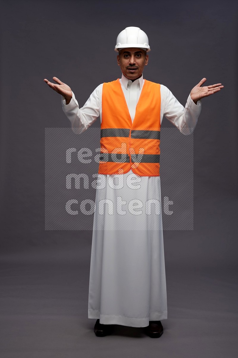 Saudi man wearing thob with engineer vest standing interacting with the camera on gray background