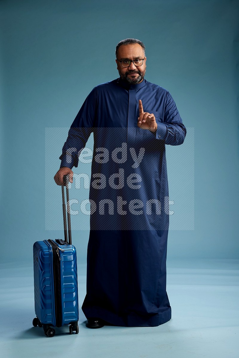 Saudi Man without shimag Standing pulling travel bag on blue background