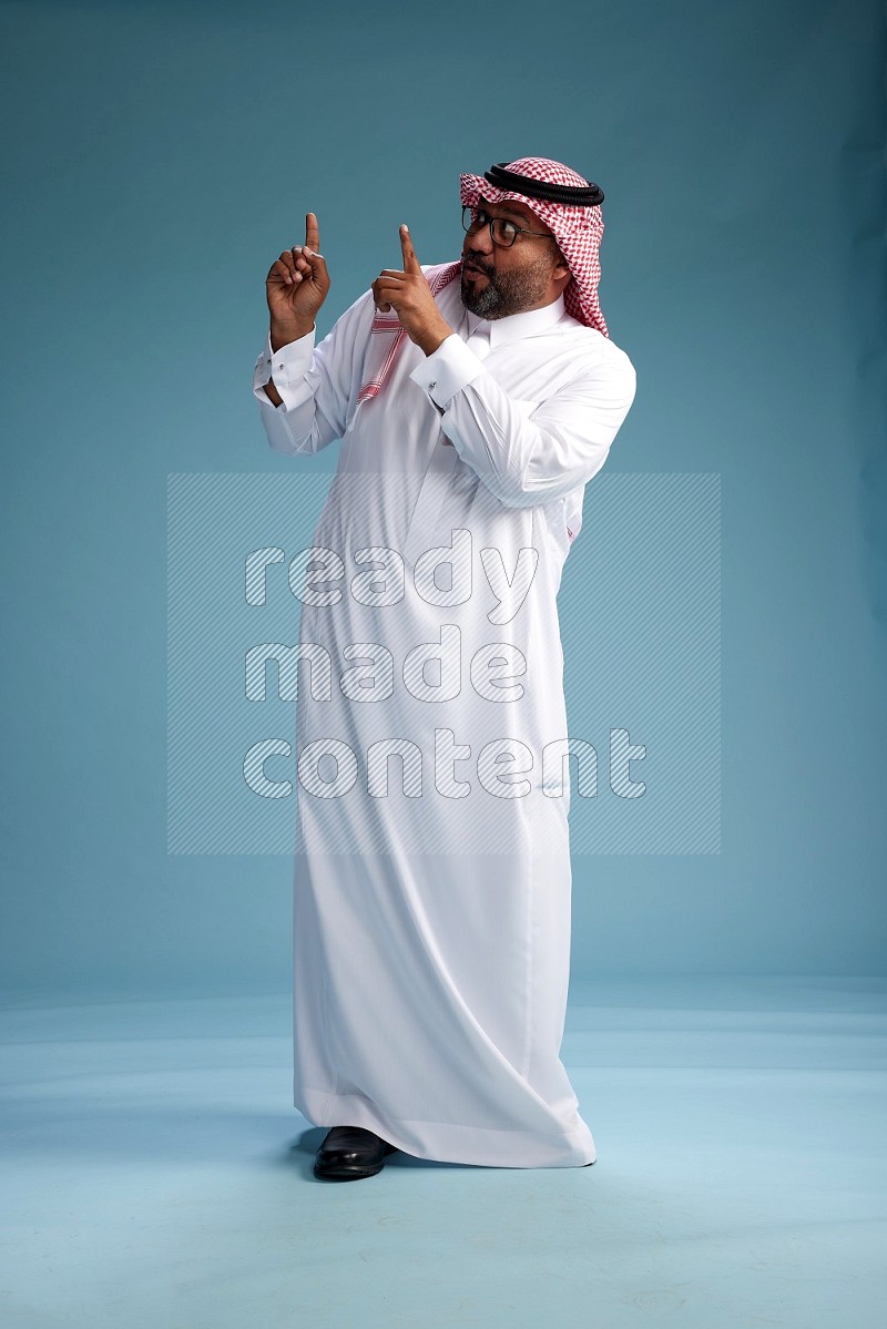 Saudi Man with shimag Standing Interacting with the camera on blue background